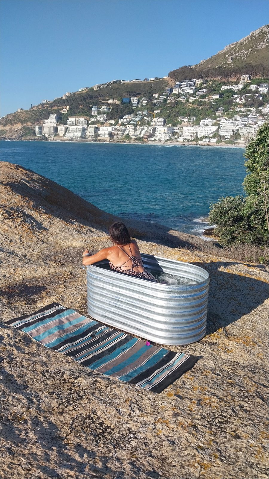 Woman in a corrugated steel ice bath overlooking Clifton beach and the Atlantic