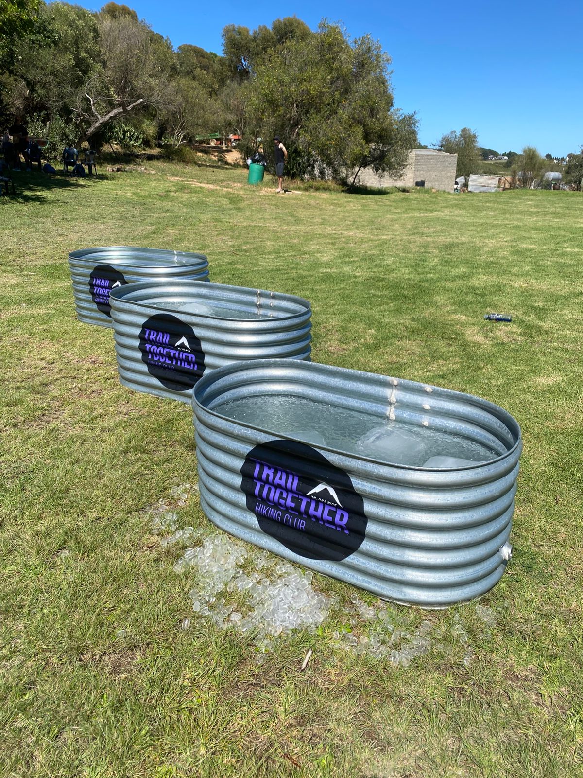 Three corrugated steel ice baths filled with ice on a grass field